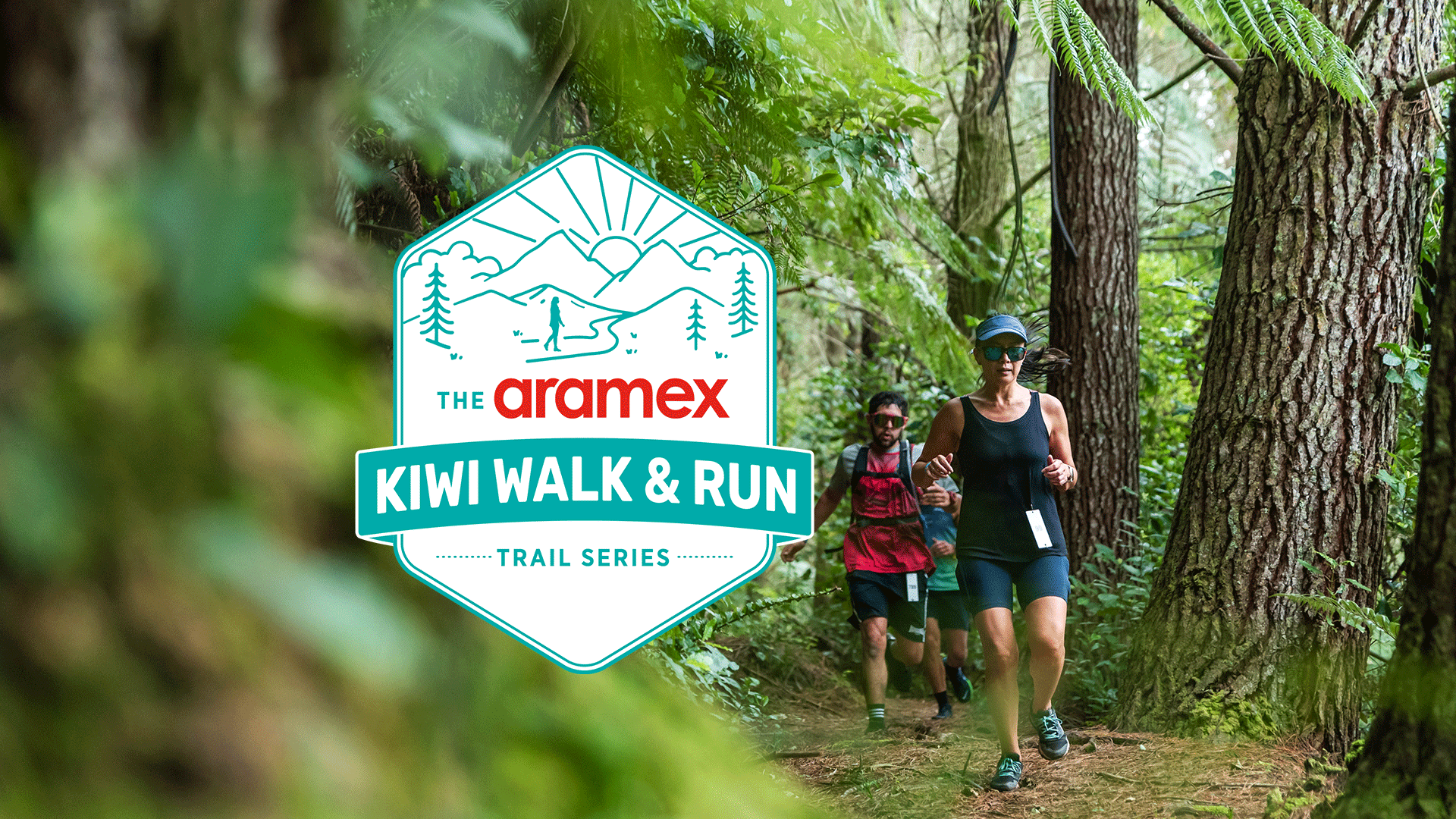 A group of people runs on a forest trail with dense green foliage, featuring the Aramex Kiwi Walk & Run Trail Series logo prominently displayed in the foreground.