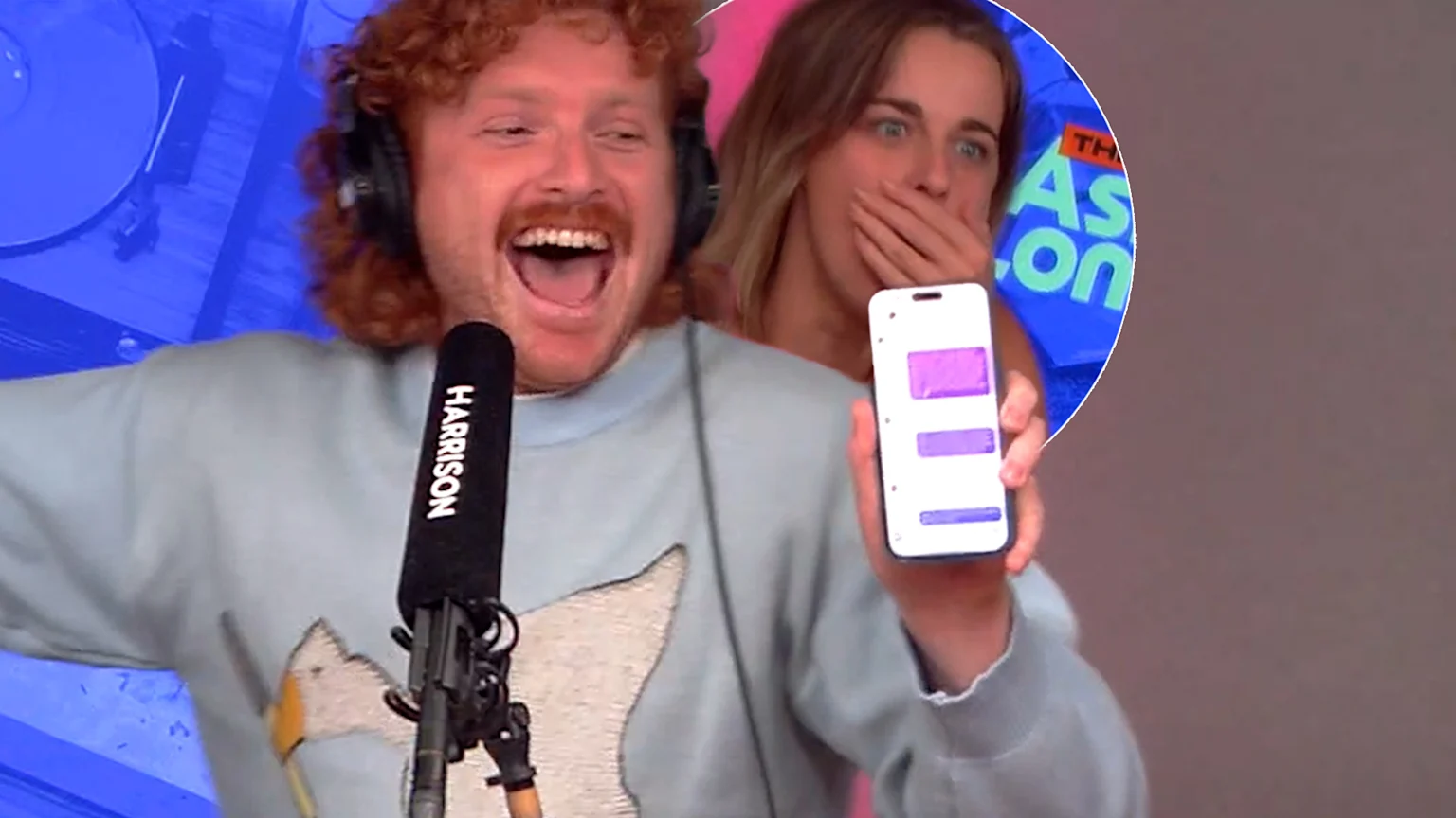 A man with red hair, wearing a light blue sweater and headphones, laughs excitedly while holding a microphone labeled HARRISON and showing a phone displaying purple messages; a woman behind him looks shocked with her hand over her mouth.