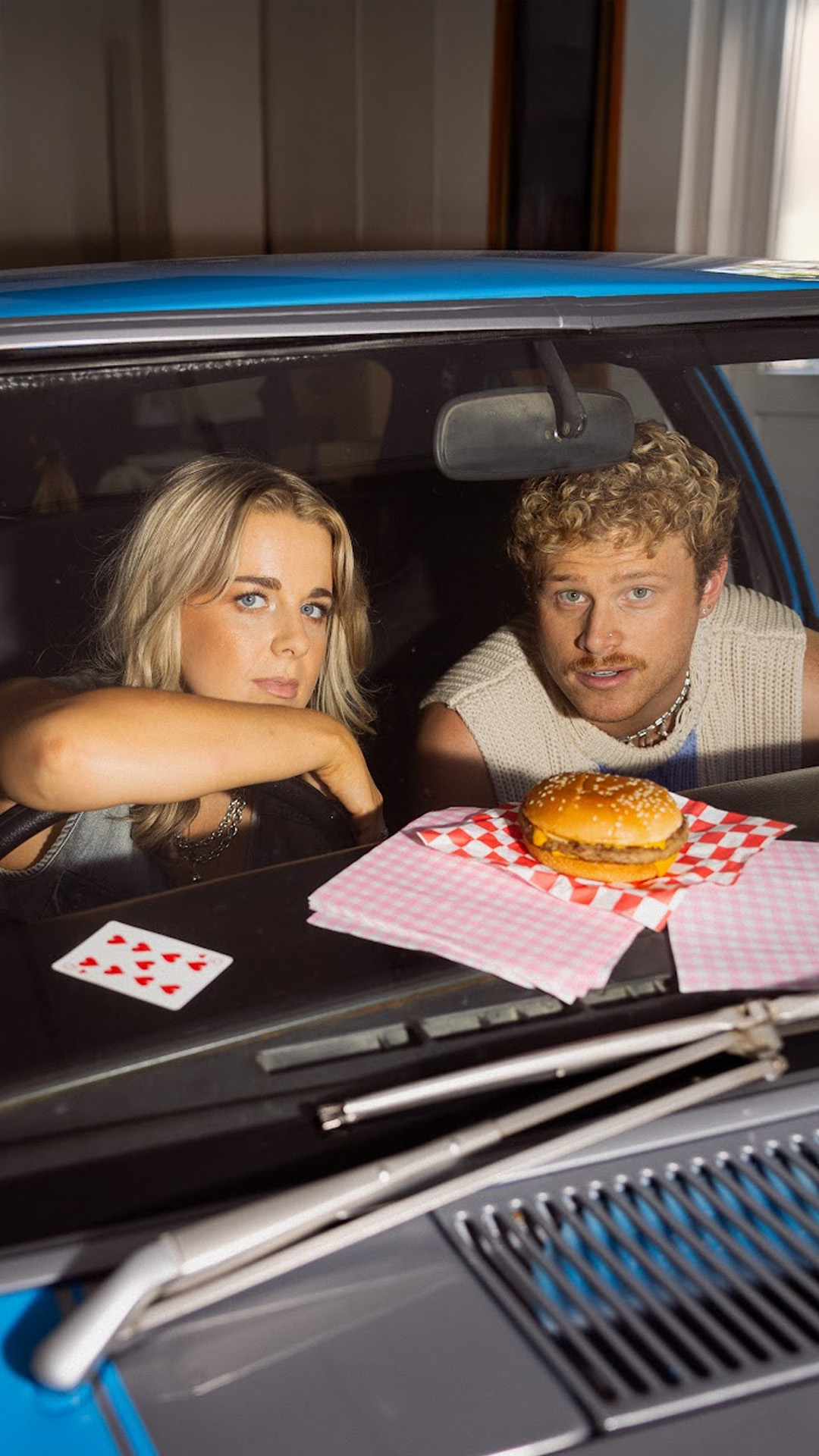 Cal and Yas in car looking at camera through windscreen