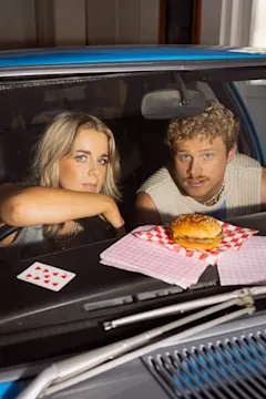 Cal and Yas in car looking at camera through windscreen