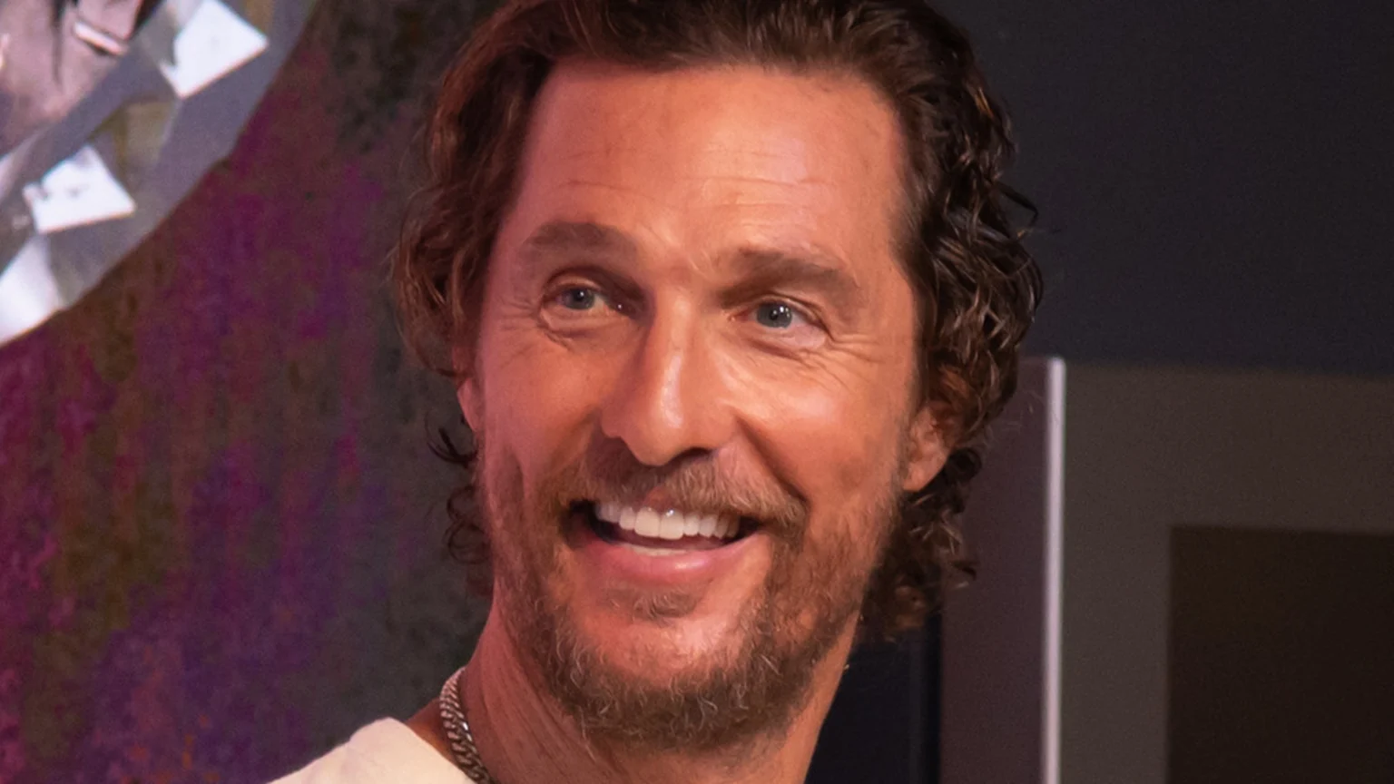 Close-up of Matthew McConaughey smiling broadly, showing his teeth, with wavy brown hair and a beard.