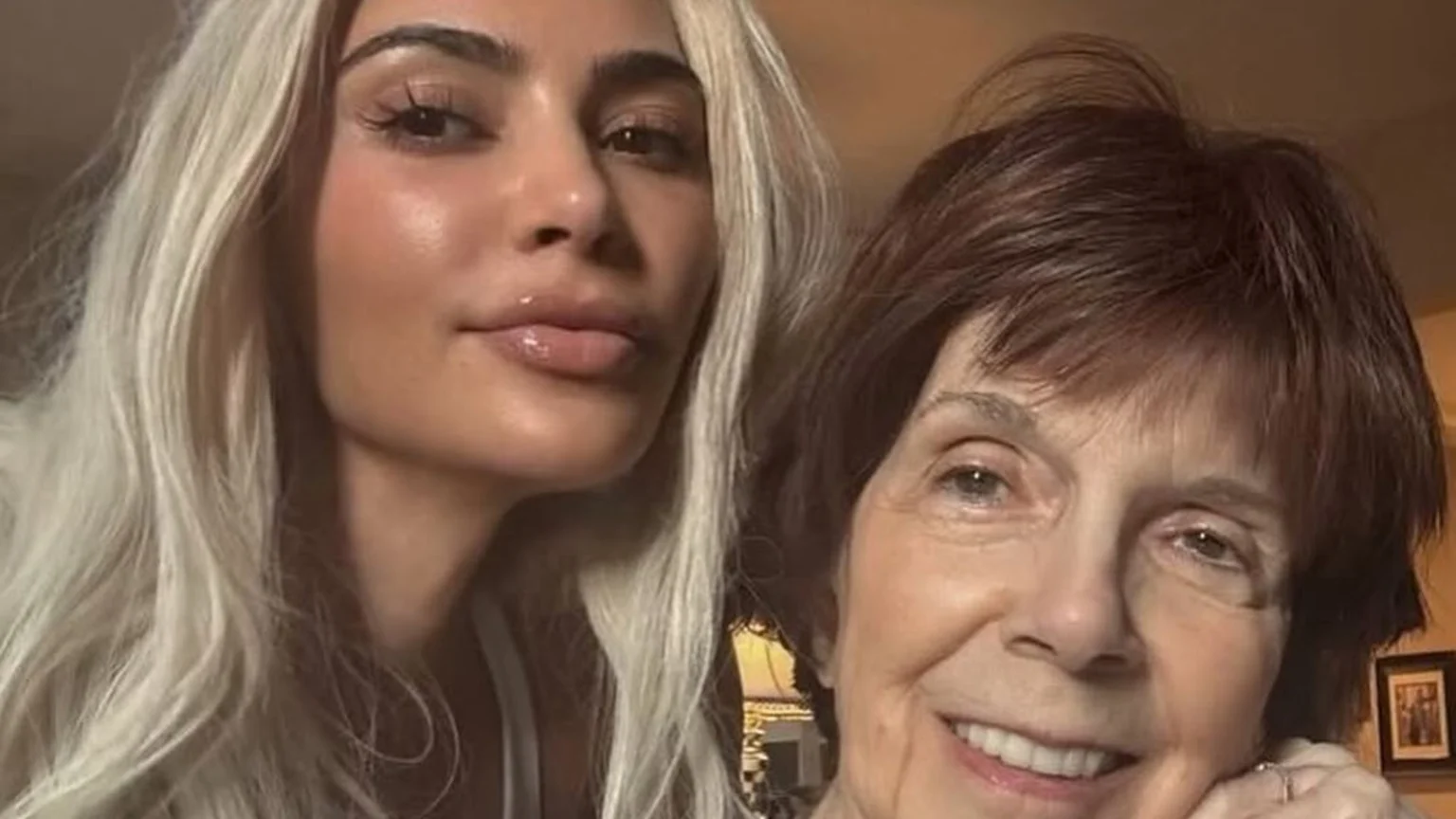 A close-up selfie shows a woman with long blonde hair and glossy lips beside an older woman with short brown hair, both smiling.