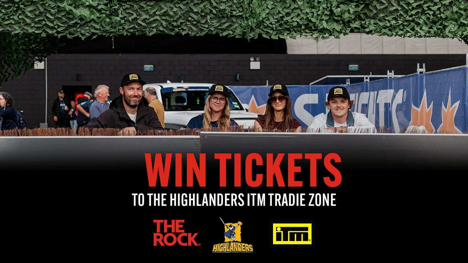 Brightly lit indoor rugby stadium with green artificial turf, white goal posts, and empty black and white seating. Advertising banners for Opulse, Southland Loan & Finance, Calder Stewart, Otago Daily Times, KFC, and more surround the field. A distant person walks on the field. Red and white overlay text promotes ticket giveaway for Highlanders ITM Tradie Zone, along with logos of The Rock, Highlanders, and ITM.