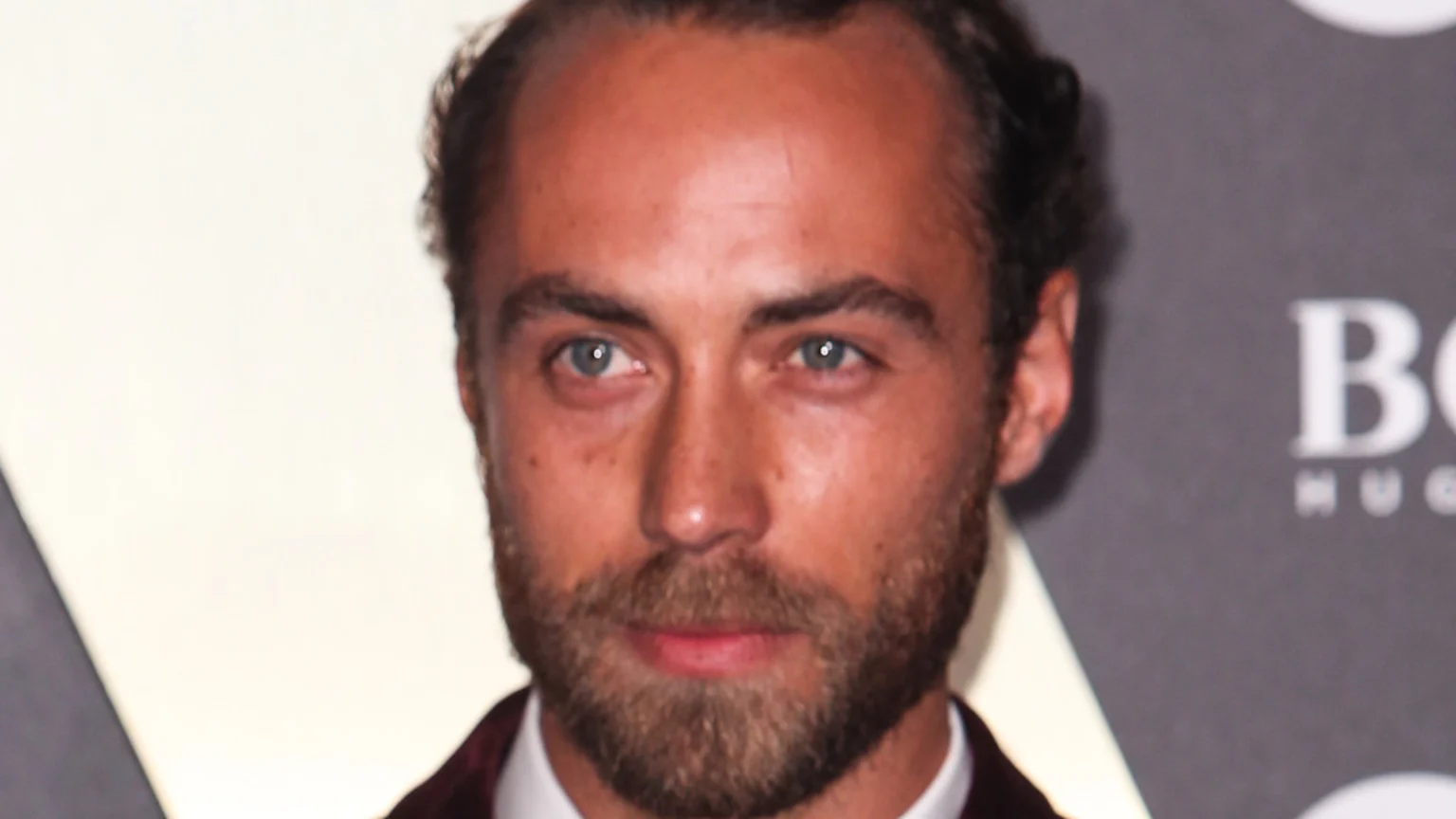 A close-up portrait of James Middleton, a man with light blue eyes and a full beard, wearing a dark jacket and white shirt, looking directly at the camera, with a blurred "BOSS" logo in the background.