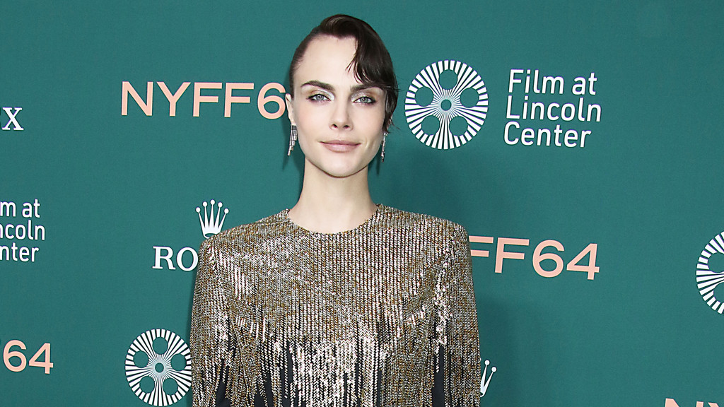 Cara Delevingne poses in a sparkly golden fringe top against a teal backdrop with "NYFF64", "Film at Lincoln Center", and "Rolex" logos.