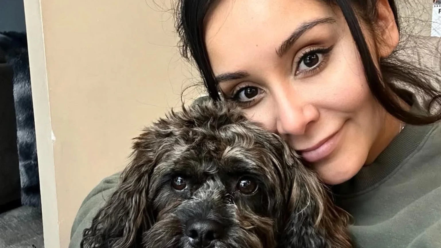 A woman with dark hair and a gentle smile holds a dark, curly-furred dog close to her, both looking softly at the viewer.