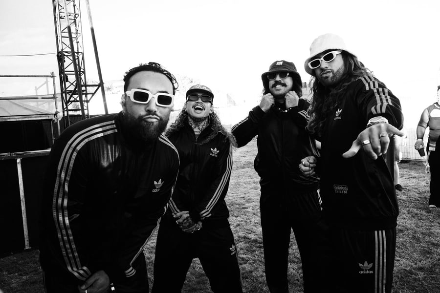 Four stylish men wearing matching Adidas tracksuits, sunglasses, and hats pose outdoors in a black and white photo.
