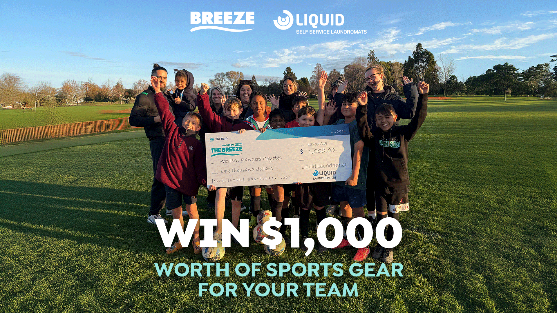 A group of happy children and adults celebrate on a grassy field, holding a large check for $1,000 from Breeze and Liquid Laundromats for sports gear, with company logos visible at the top.