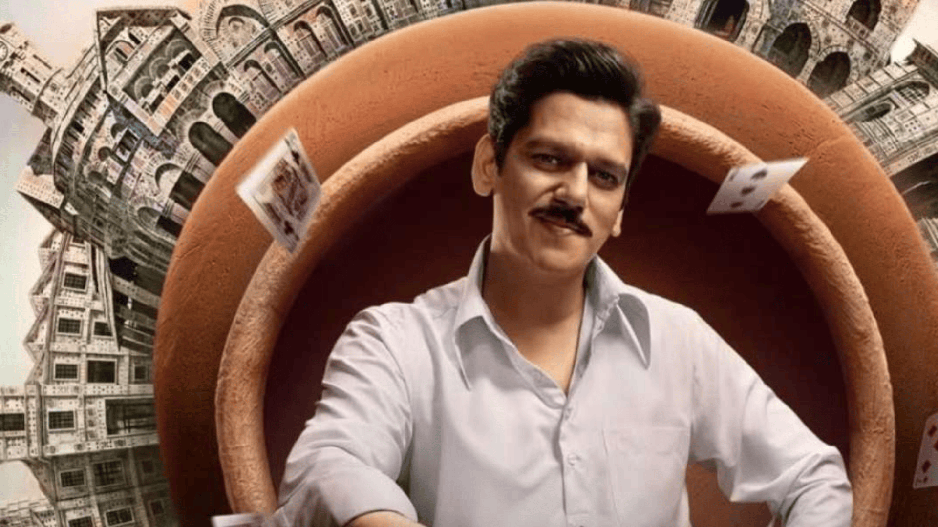 A smiling man with a mustache wears a white shirt, framed by a large brown ring, with playing cards floating around him and intricate city structures in the background.