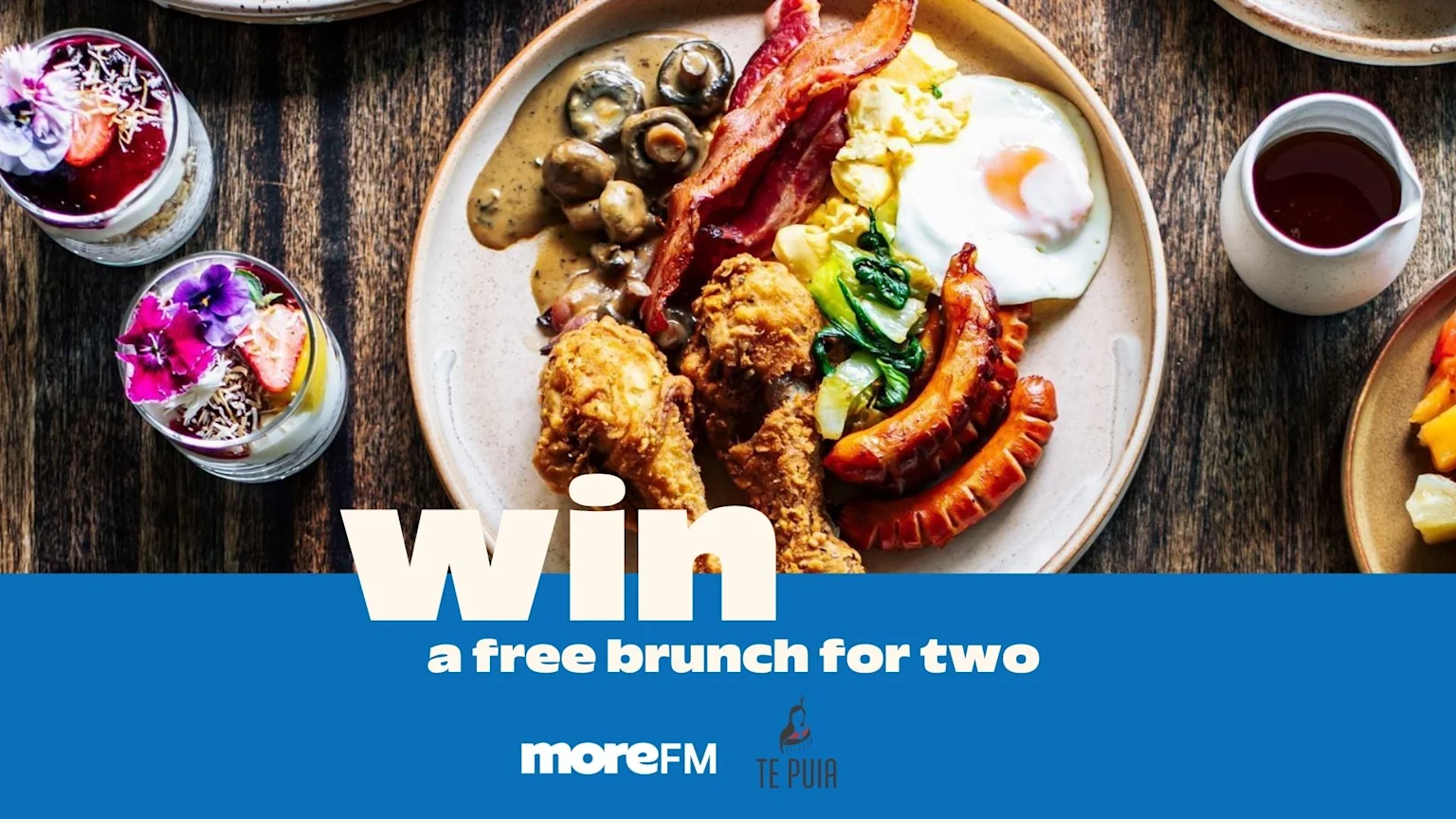 A top-down view of a large brunch plate with fried chicken, sausages, bacon, eggs, and mushrooms, plus two dessert parfaits and a blue banner promoting "Win a free brunch for two".