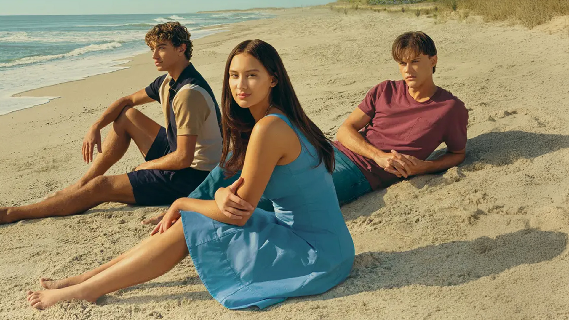 Four individuals, two men and two women, stand side-by-side against a blue background featuring parts of a title in white letters, likely "THE SUMMER I TURNED PRETTY".