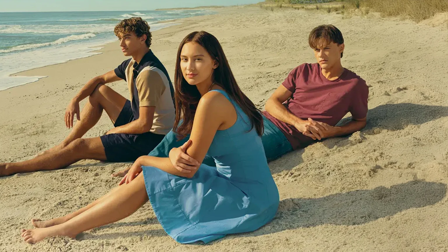Four individuals, two men and two women, stand side-by-side against a blue background featuring parts of a title in white letters, likely "THE SUMMER I TURNED PRETTY".