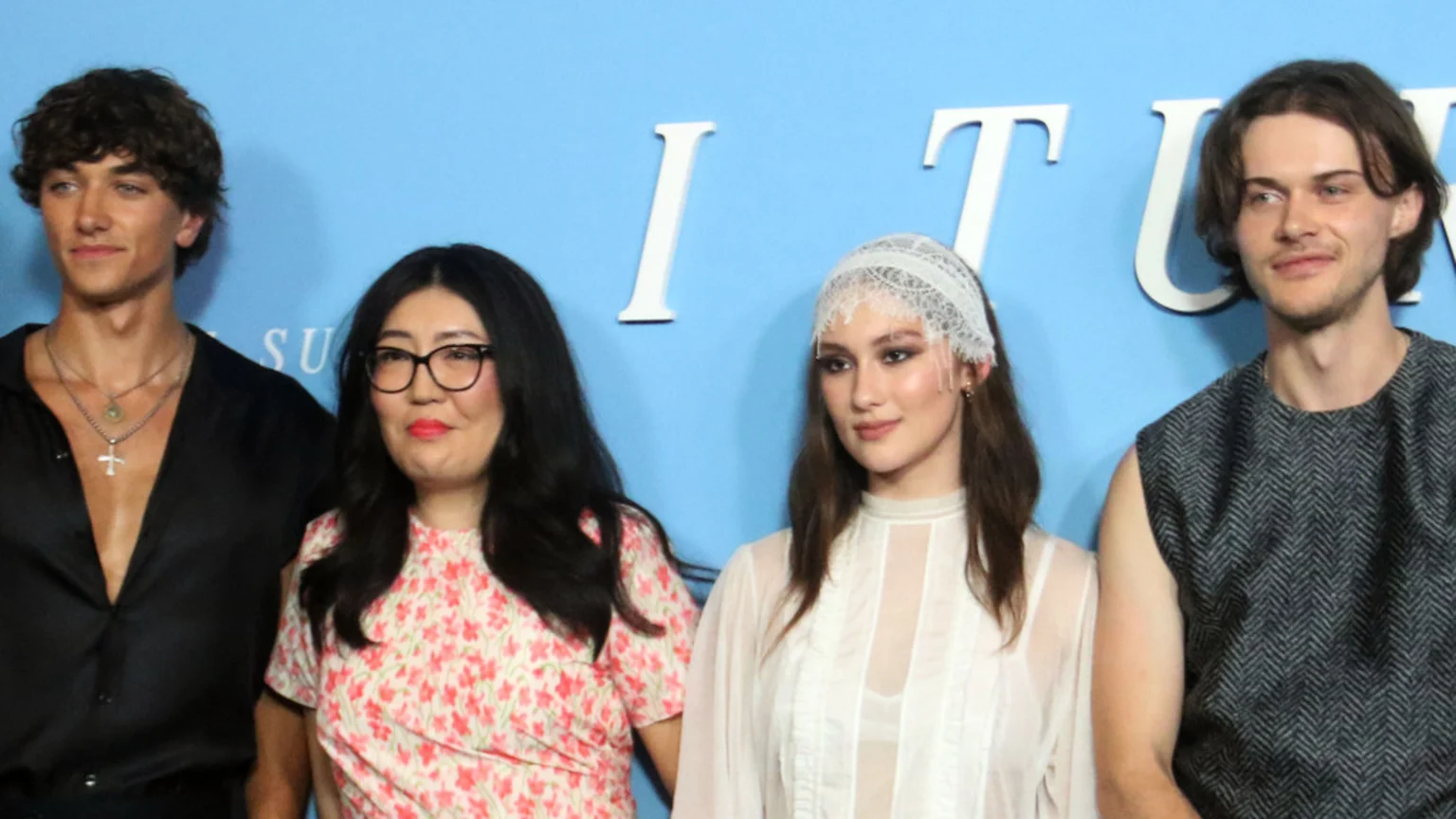 Four individuals, two men and two women, stand side-by-side against a blue background featuring parts of a title in white letters, likely "THE SUMMER I TURNED PRETTY".