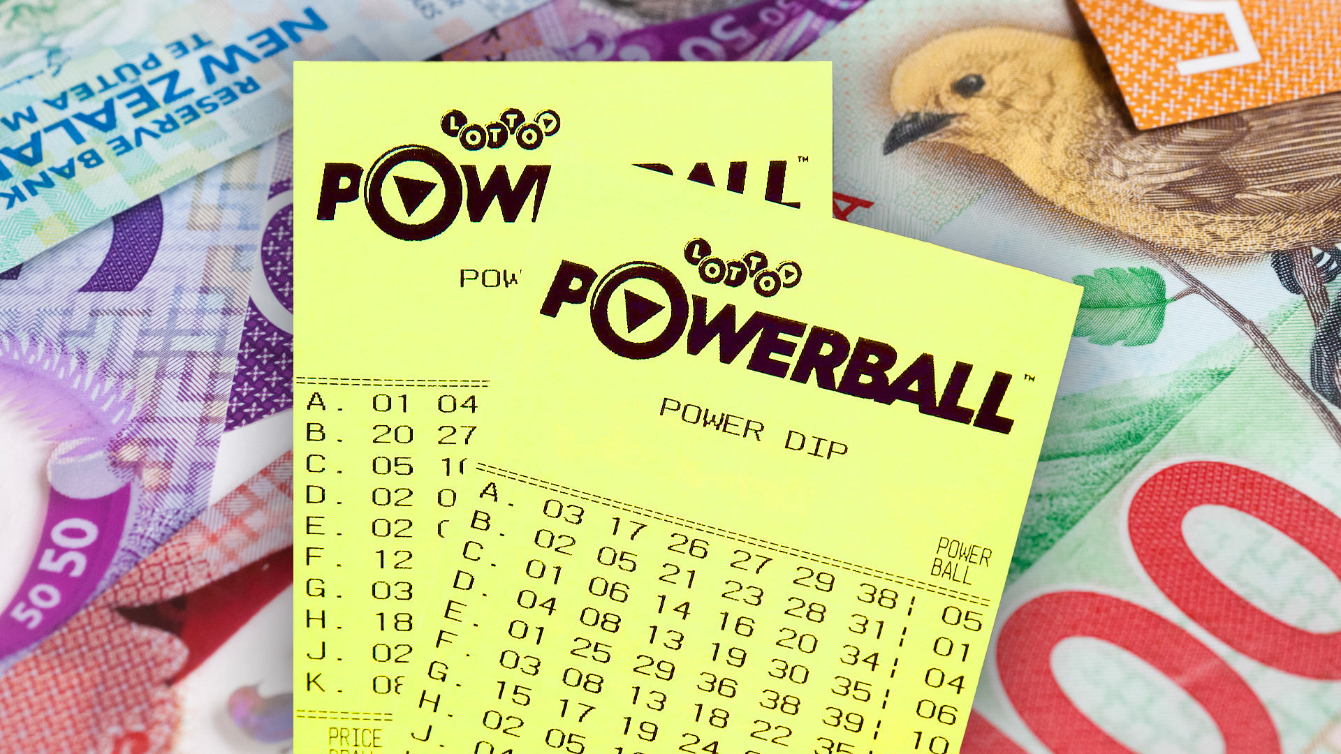 Two yellow New Zealand Powerball lottery tickets are fanned over a spread of colorful New Zealand banknotes, including a $50 note with a bird.