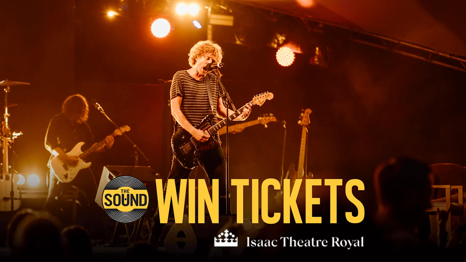 A band performs live on stage under warm lights, with a lead singer playing an electric guitar, alongside "THE SOUND" logo, "WIN TICKETS" text, and "Isaac Theatre Royal" branding.