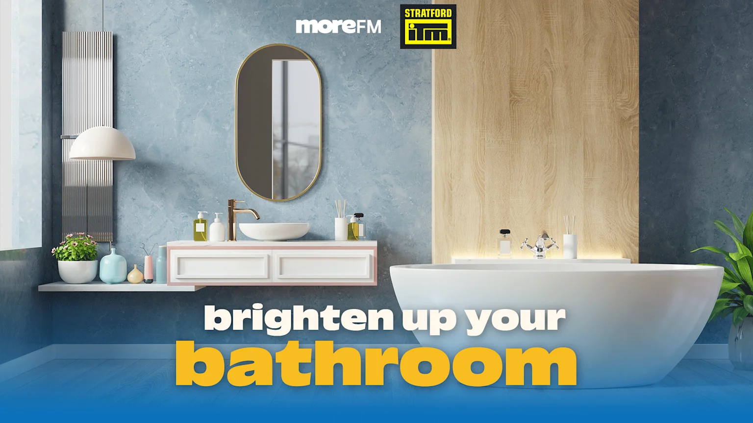 A modern bathroom with a white freestanding tub, floating vanity, gold faucet, oval mirror, light blue walls, and wood paneling, encouraging to 'brighten up your bathroom' with MoreFM and Stratford IM logos.