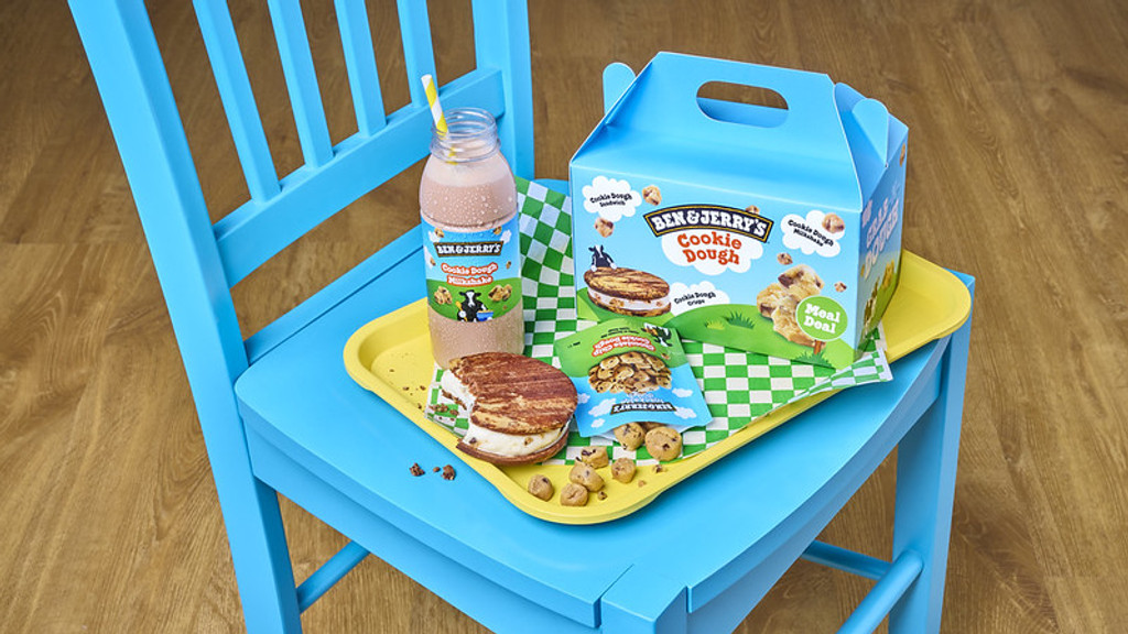 A Ben & Jerry's Cookie Dough meal deal, including a blue box, milkshake, ice cream sandwich, and cookie dough bites, is on a yellow tray on a blue chair.