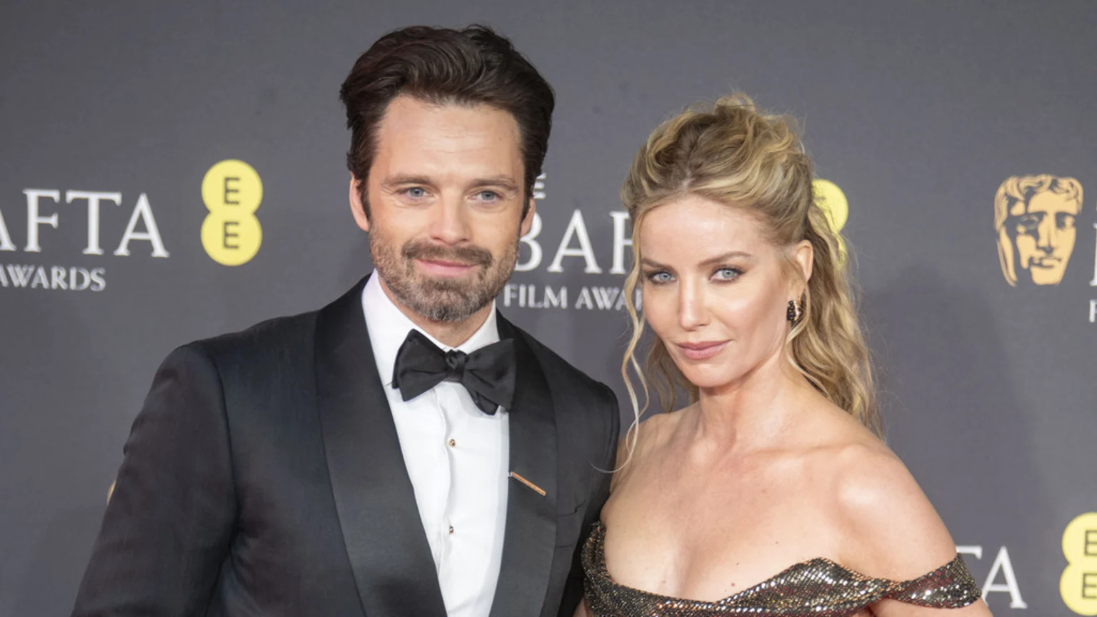 Sebastian Stan in a black tuxedo and Annabelle Wallis in a sparkling, off-the-shoulder gown pose together at a BAFTA Film Awards event.