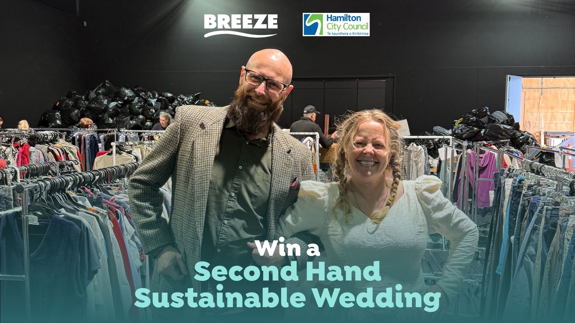 A smiling man and woman stand in a second-hand store filled with clothing racks and piles of black bags, promoting a sustainable wedding.