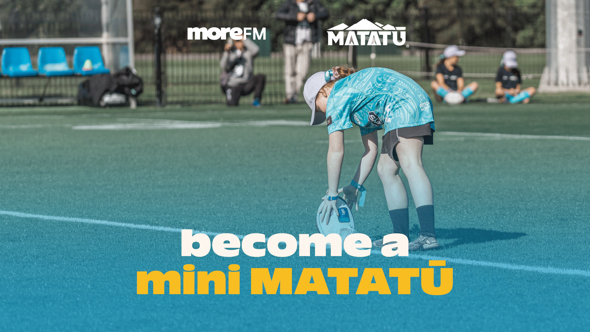 A young girl in a blue Matatū rugby jersey places a white rugby ball on a green turf field, with sponsor logos and "become a mini MATATŪ" text at the bottom.