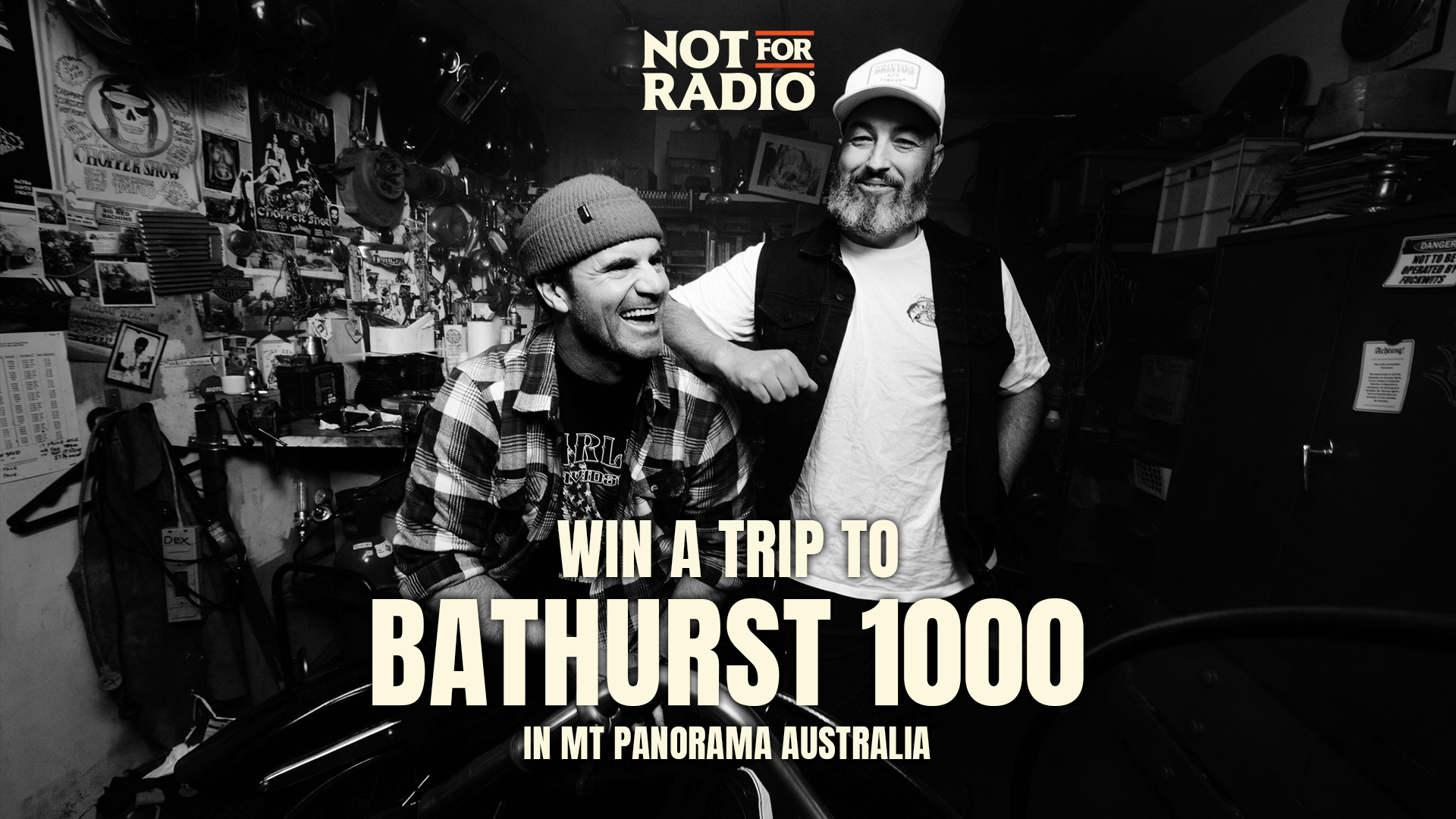 Two smiling men, one in a beanie and plaid shirt and the other in a cap and vest, stand in a workshop with "WIN A TRIP TO BATHURST 1000" overlay text.