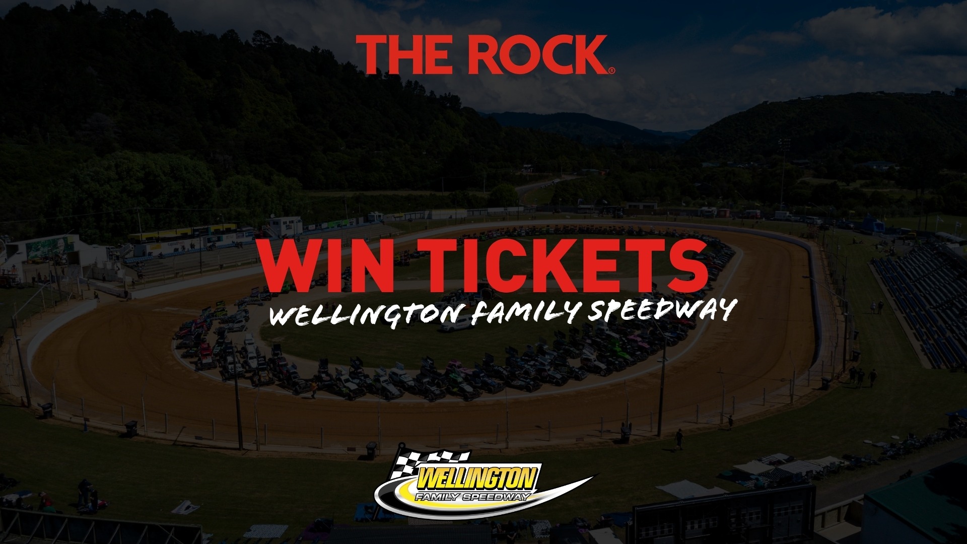 Aerial view of Wellington Family Speedway with many race cars on a dirt track, grandstands, and green hills, featuring "THE ROCK" and "WIN TICKETS" text overlays.