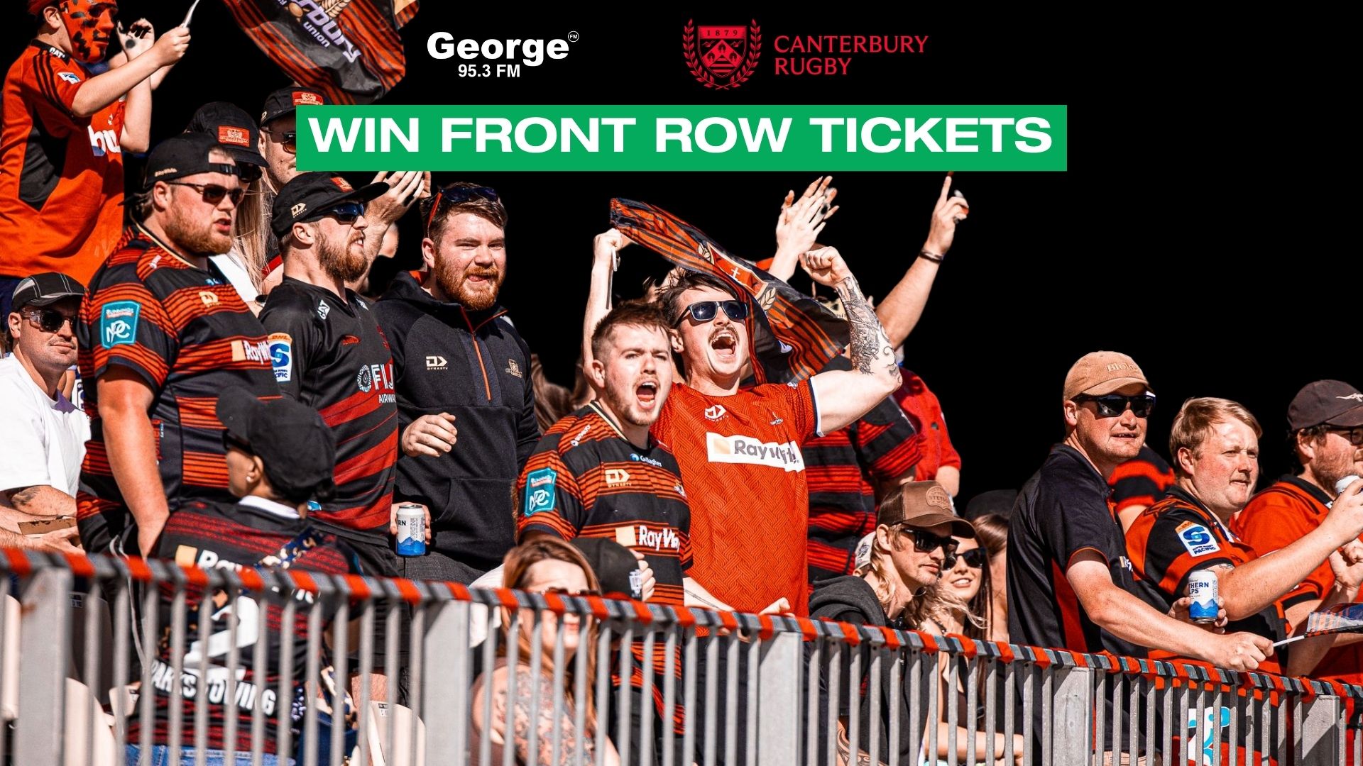 A large group of excited rugby fans, mostly men in red and black jerseys, cheer enthusiastically in a stadium with a dark background, while a banner advertises "WIN FRONT ROW TICKETS."