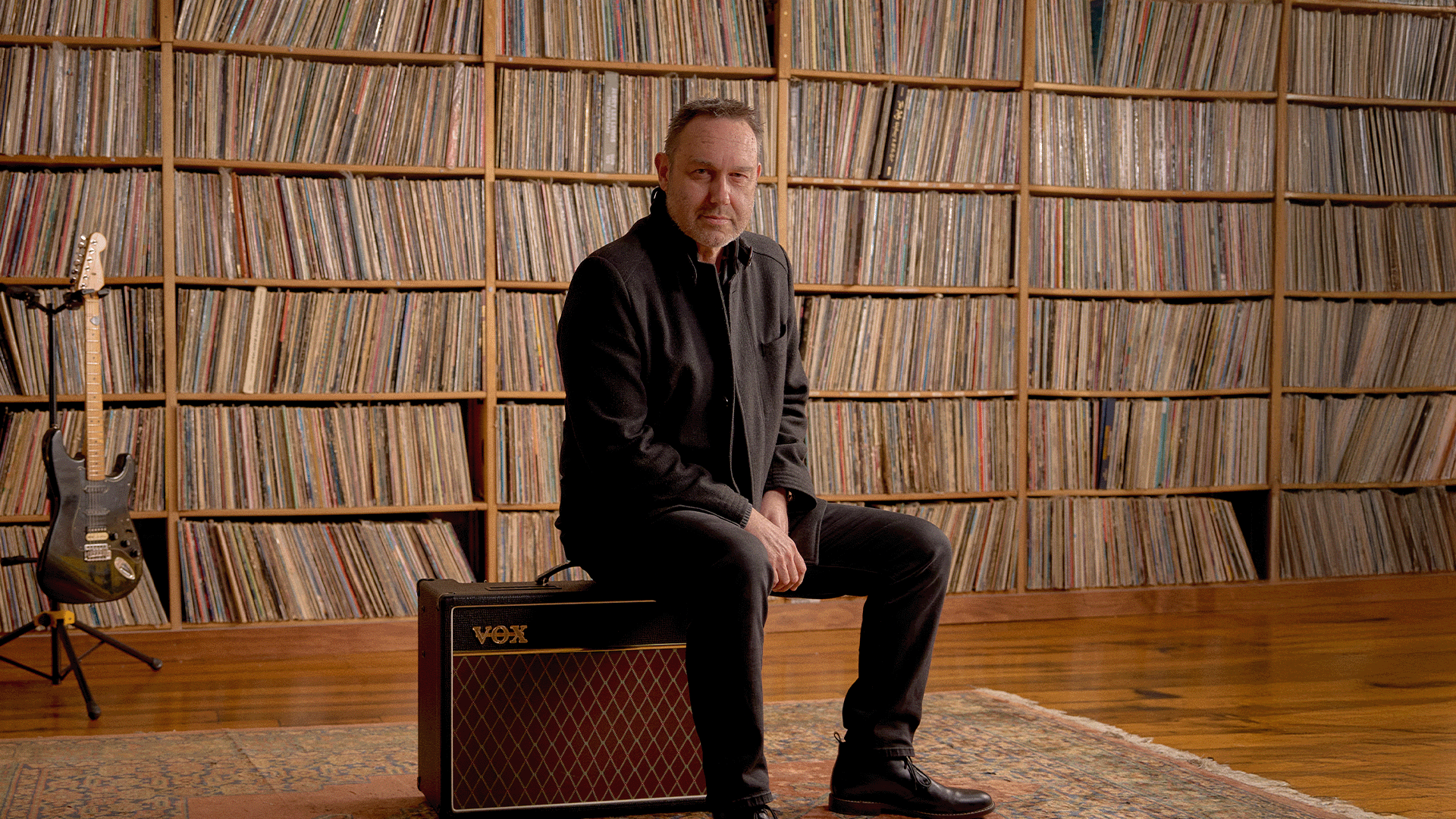 Mark 'Woodsie' Hazelwood sits on VOX amp in front of vinyl record collection wall