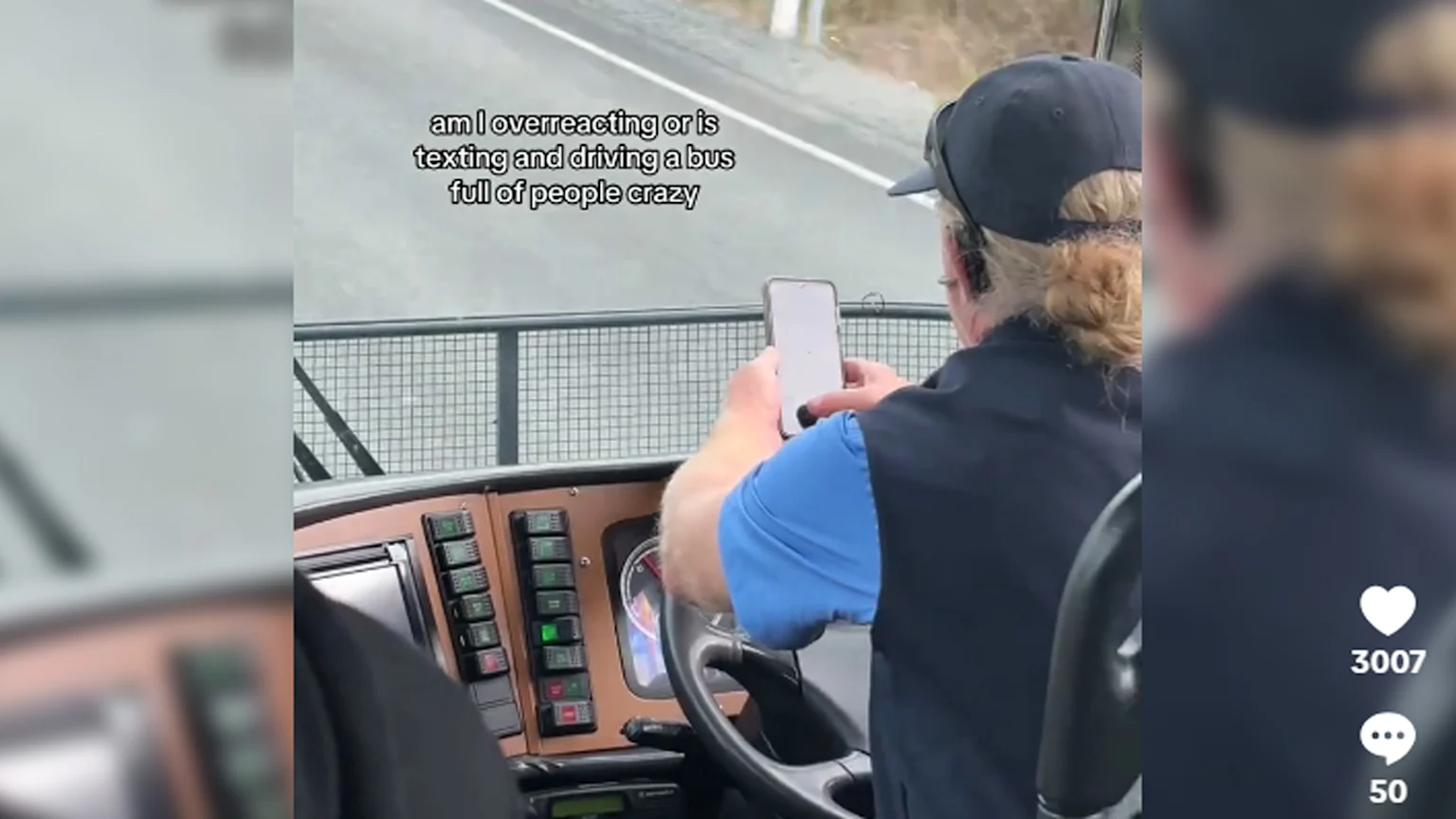 A bus driver, seen from behind, holds a smartphone with both hands while operating the steering wheel, with the dashboard controls and a road visible ahead.