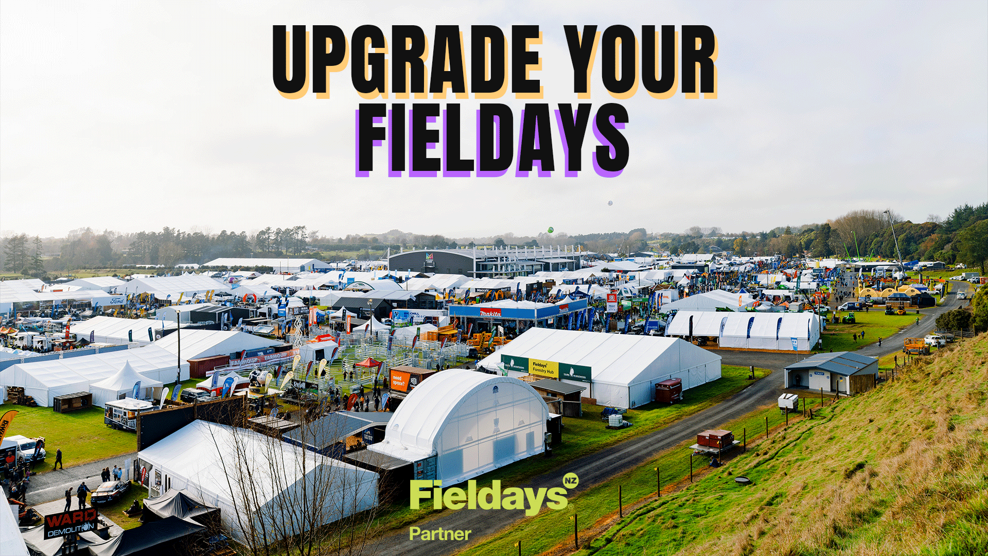An aerial view of the bustling outdoor Fieldays event, showcasing numerous white tents, trade displays, equipment, and visitors, with text "UPGRADE YOUR FIELDDAYS" and "Fieldays® NZ Partner."