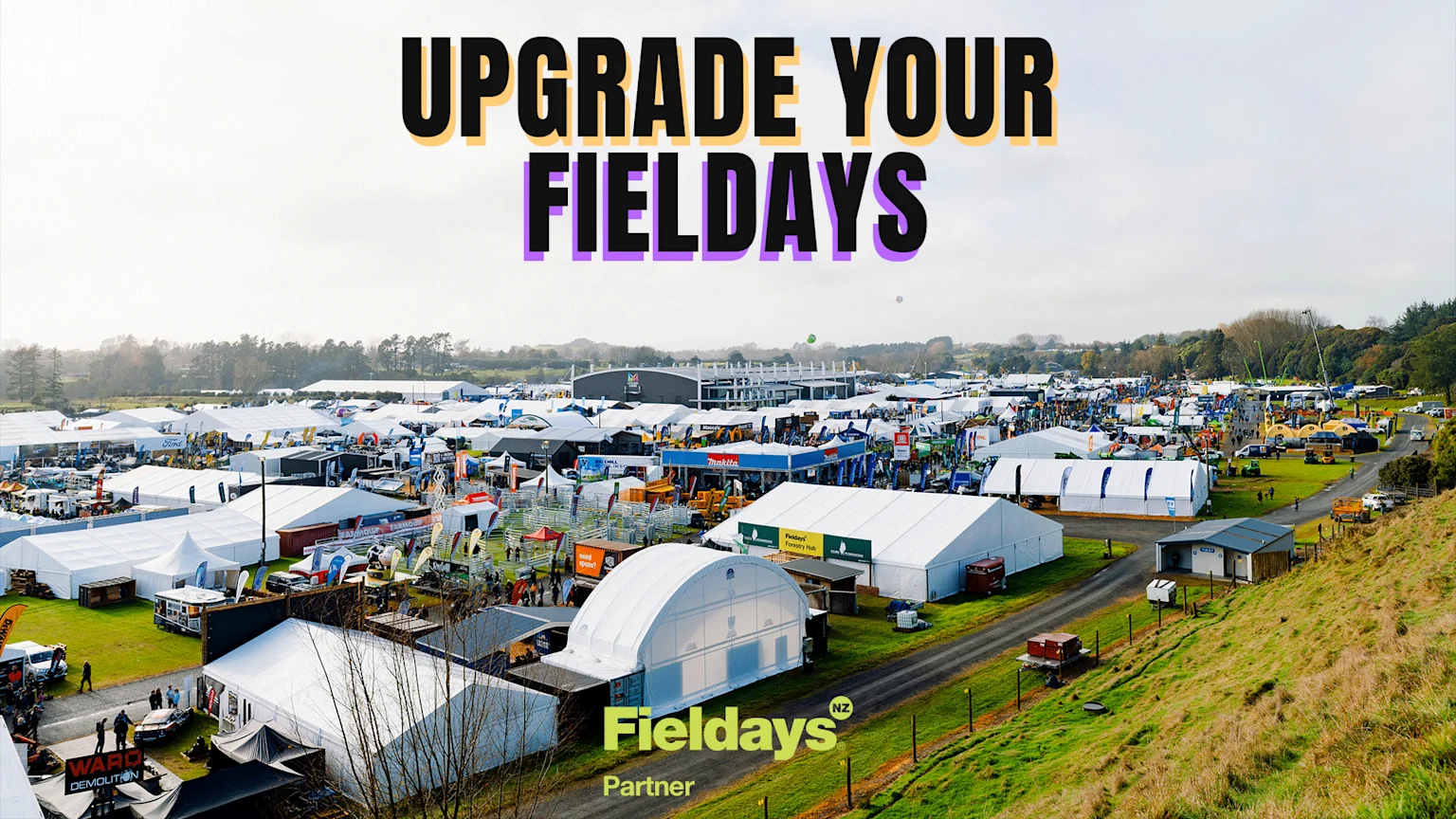 An aerial view of the bustling outdoor Fieldays event, showcasing numerous white tents, trade displays, equipment, and visitors, with text "UPGRADE YOUR FIELDDAYS" and "Fieldays® NZ Partner."
