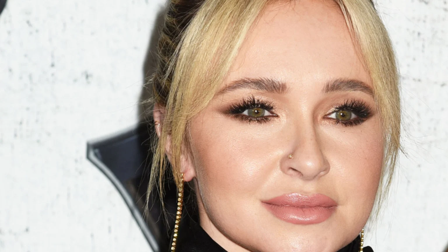 Close-up of Hayden Panettiere, featuring her blonde hair, green eyes with prominent eyelashes, a small nose piercing, and light pink lipstick.