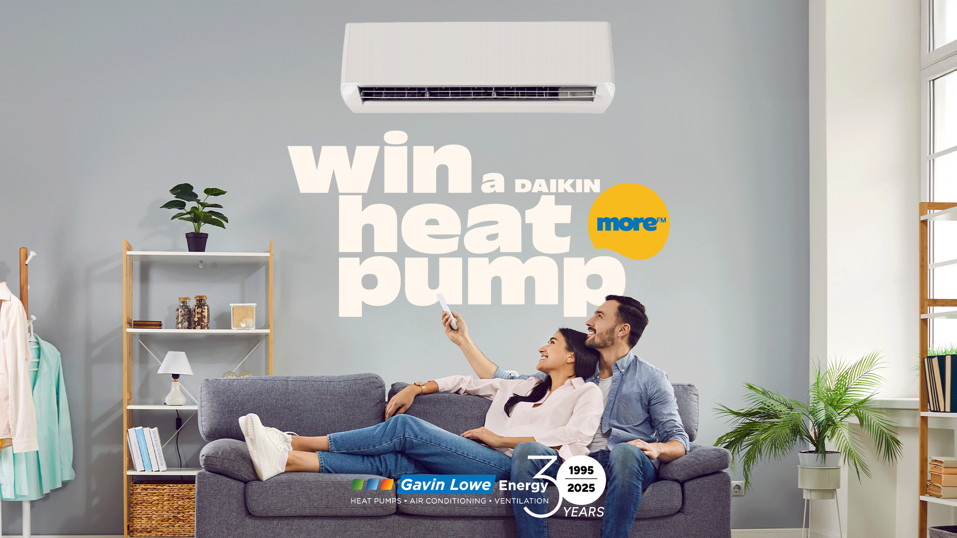 A smiling couple on a sofa looks up at a wall-mounted heat pump, with text "win a DAIKIN heat pump" and "Gavin Lowe Energy" branding in a modern living room.