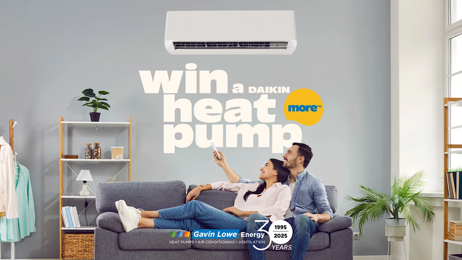 A smiling couple on a sofa looks up at a wall-mounted heat pump, with text "win a DAIKIN heat pump" and "Gavin Lowe Energy" branding in a modern living room.