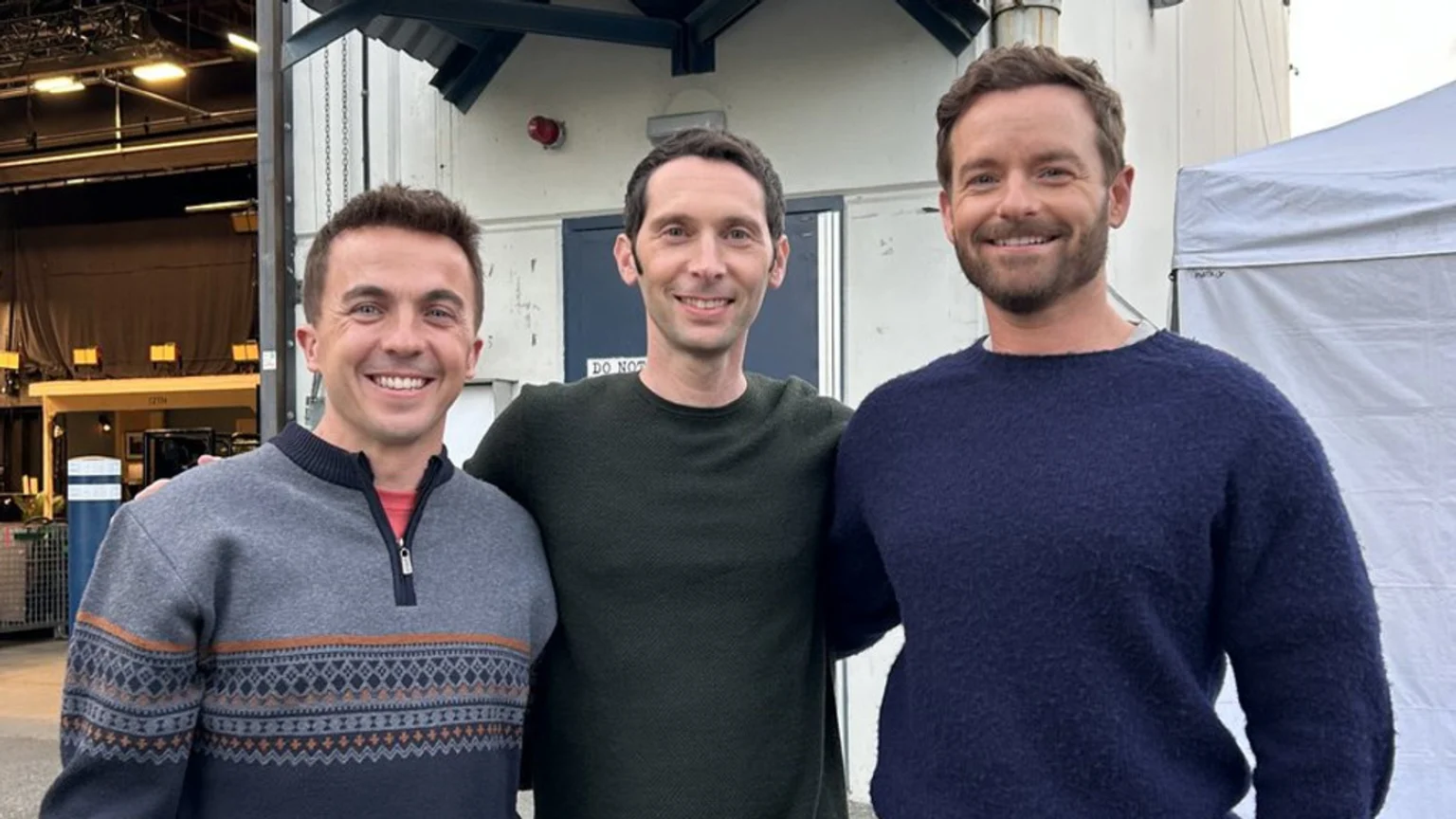 Frankie Muniz, Justin Berfield, and Chris Masterson smile while standing side-by-side outdoors.
