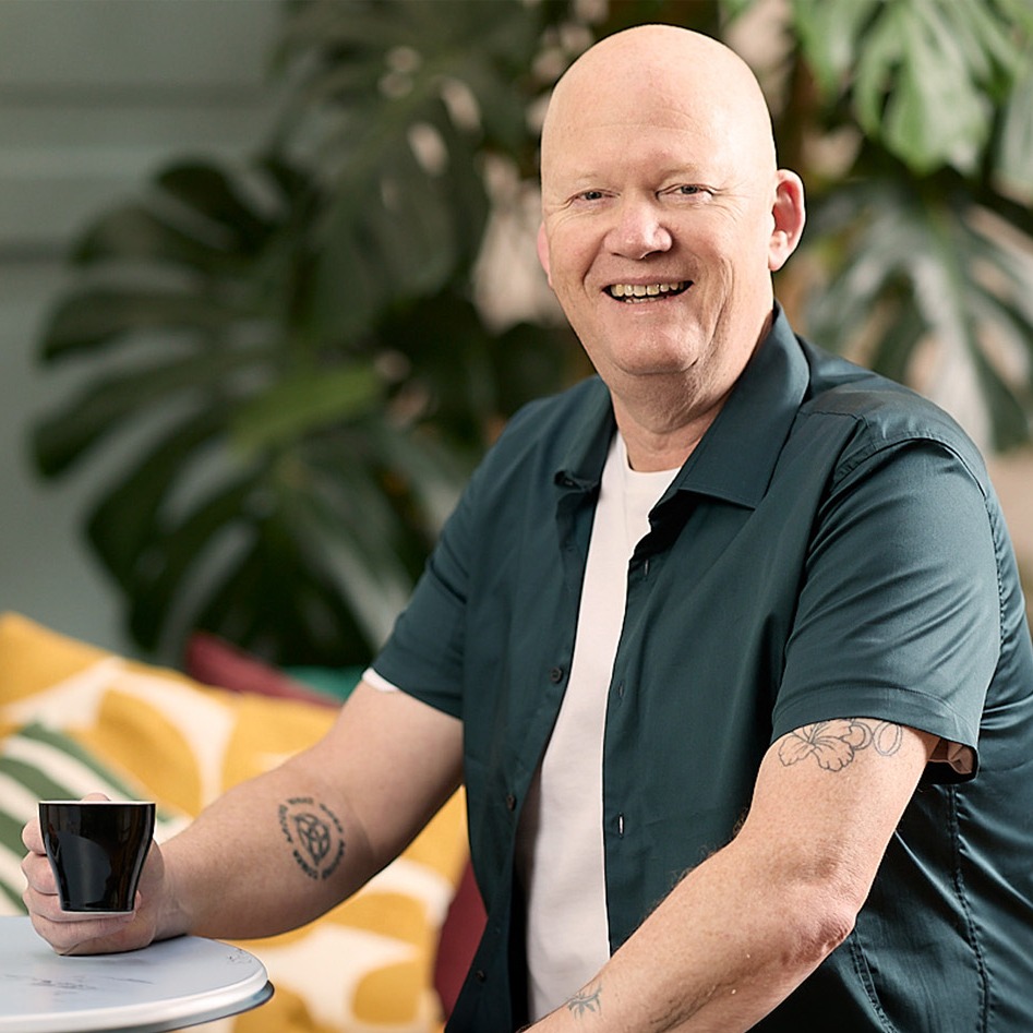Martin Good sitting in colourful lounge drinking tea