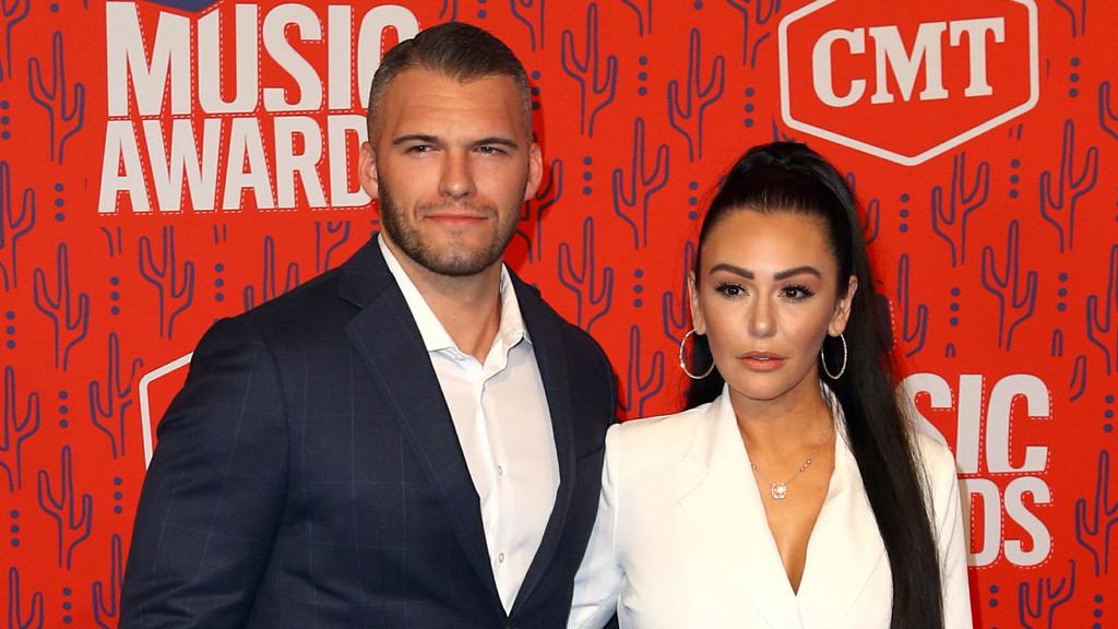 Reality TV star Jenni 'JWoww' Farley in a white blazer and a man in a blue suit pose for a photo against a red background with cactus patterns and 'MUSIC AWARD' text.