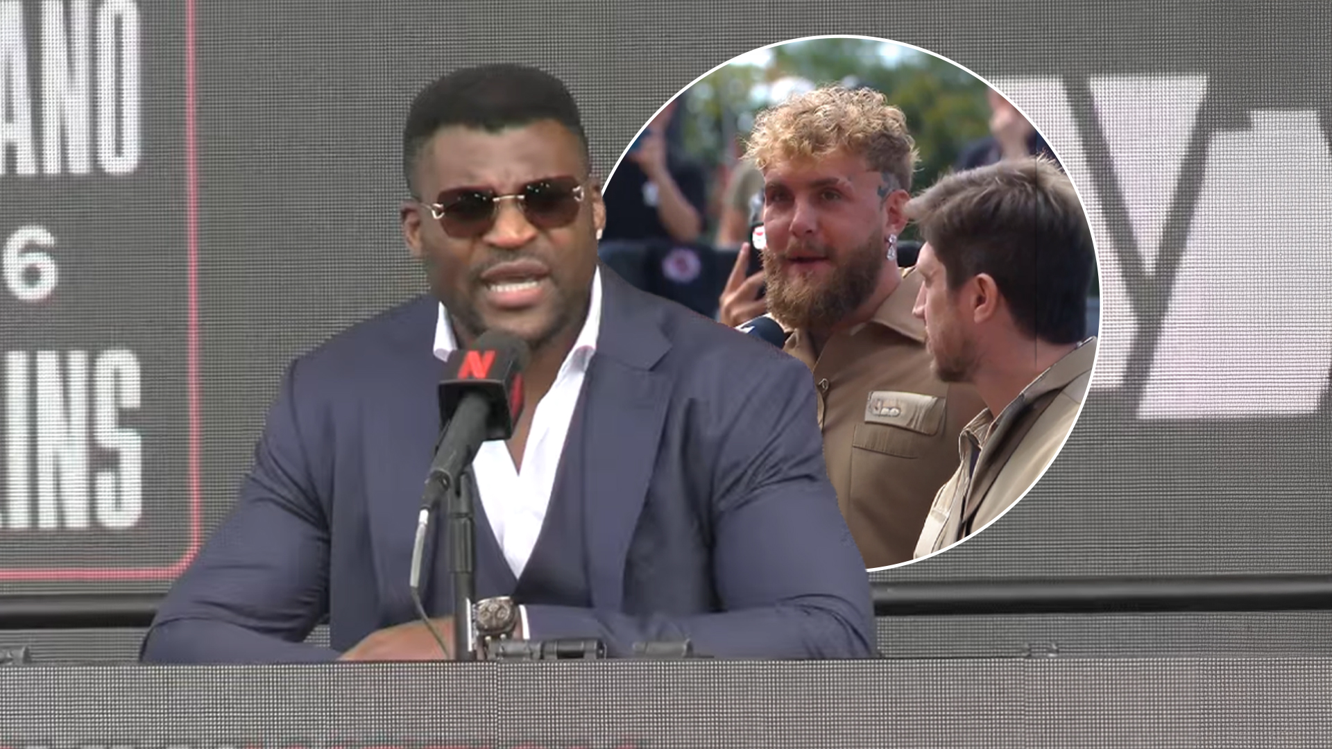 Francis Ngannou, wearing a dark suit and sunglasses, speaks into a microphone, with a circular inset showing Jake Paul with curly blonde hair and a beard talking to another man.