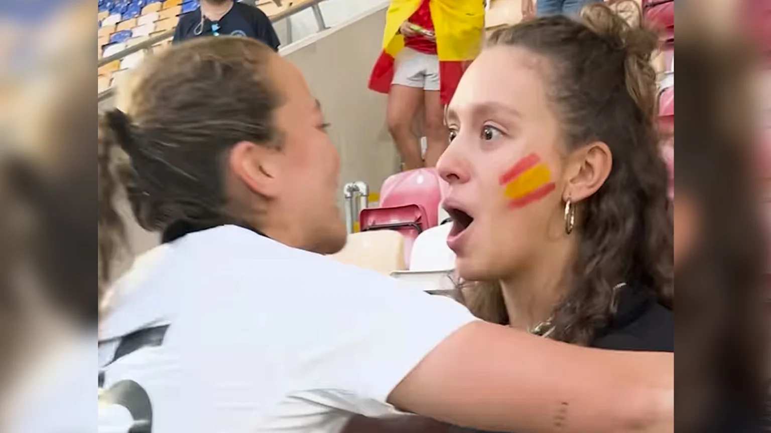 Spanish rugby fan wearing All Blacks jersey and has Spain flags painted on cheeks looks shocked as Black Fern player, Renee Holmes, goes in for a hug.