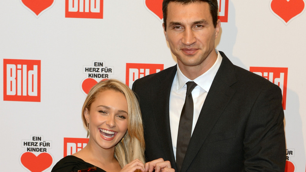 Wladimir Klitschko in a black suit smiles while standing next to Hayden Panettiere, who is laughing with her mouth open, against a white background with red "Bild" and "Ein Herz für Kinder" logos.