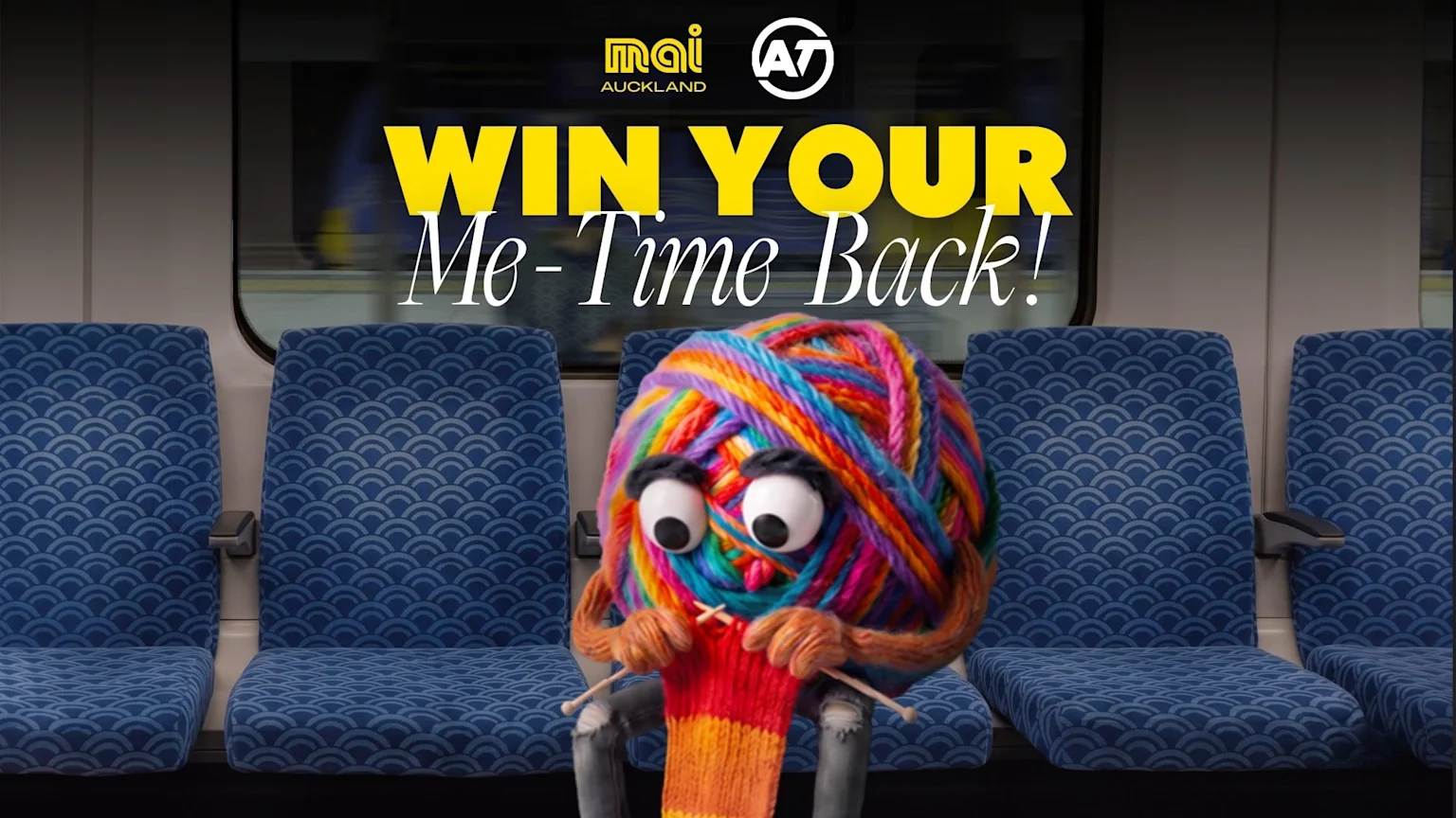 A colorful yarn character with googly eyes knits on a train seat under the text "WIN YOUR Me-Time Back!", with Mai Auckland and AT logos visible.