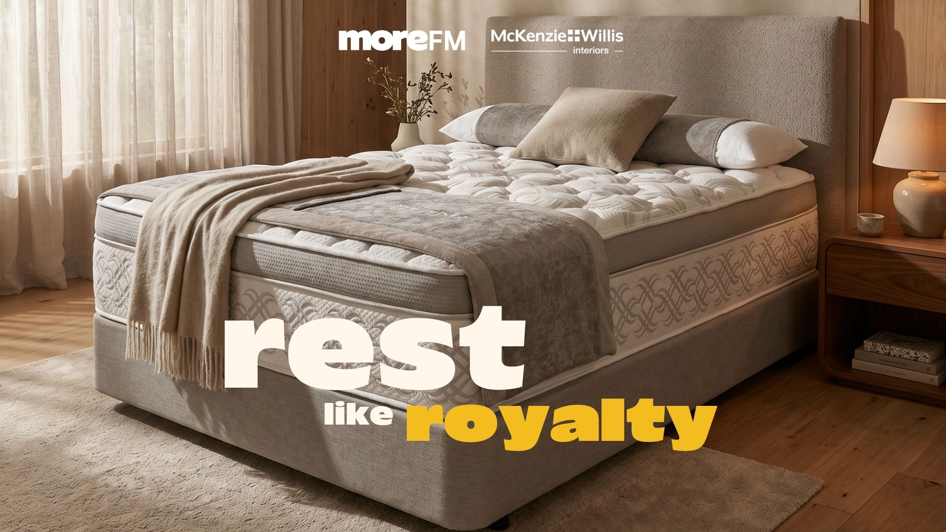 A luxurious king-size bed with multiple layers of mattresses, a patterned border, a grey upholstered headboard, and soft beige bedding, in a light bedroom.