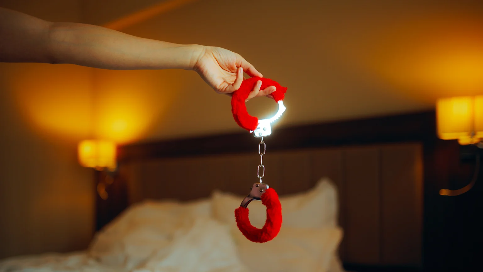 Hand holding pair of fluffy red handcuffs
