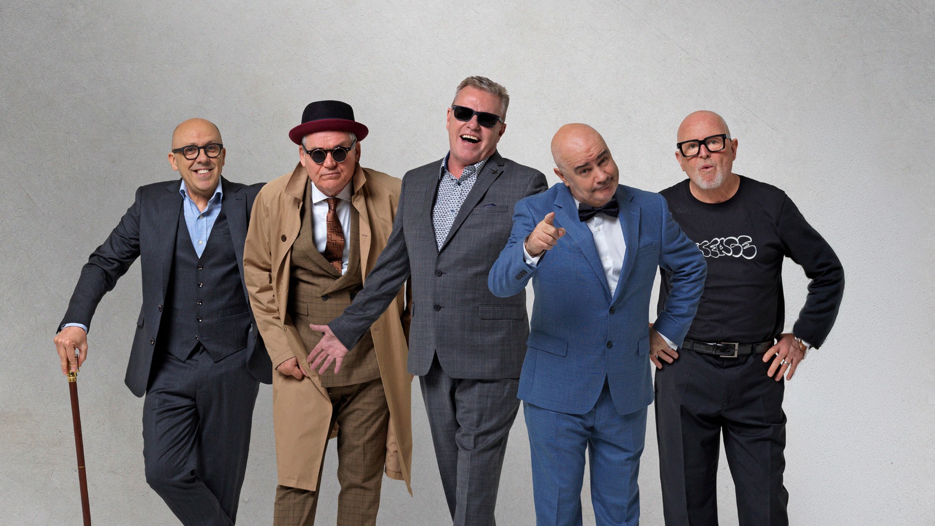 Five smiling bald men in a mix of smart and casual attire, posing against a light background.