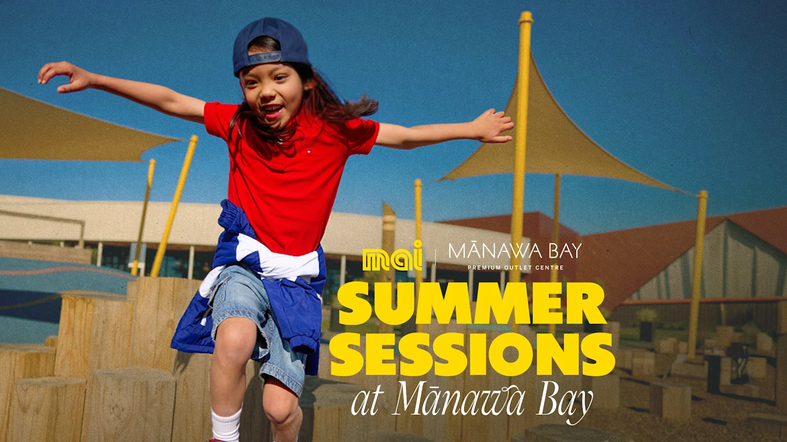 Kid in red shirt and denim shorts with cap jumping off playground. "Summer Sessions at Mānawa Bay" with Mai FM Auckland