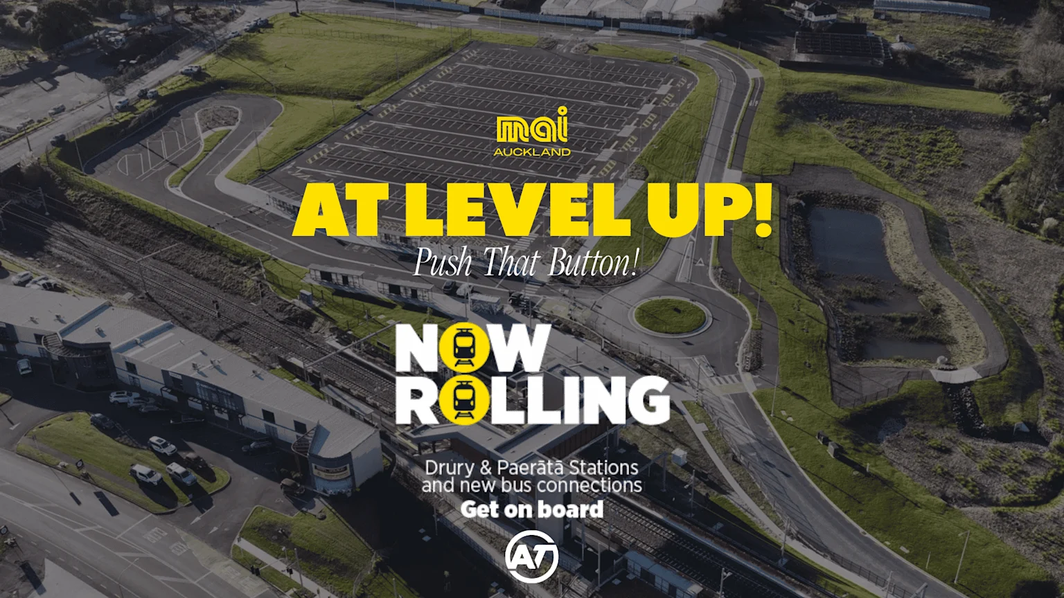 Aerial drone shot of a newly developed train station with tracks, a large parking lot, roads including a roundabout, and surrounding green areas, with overlaid text announcing new transport services.