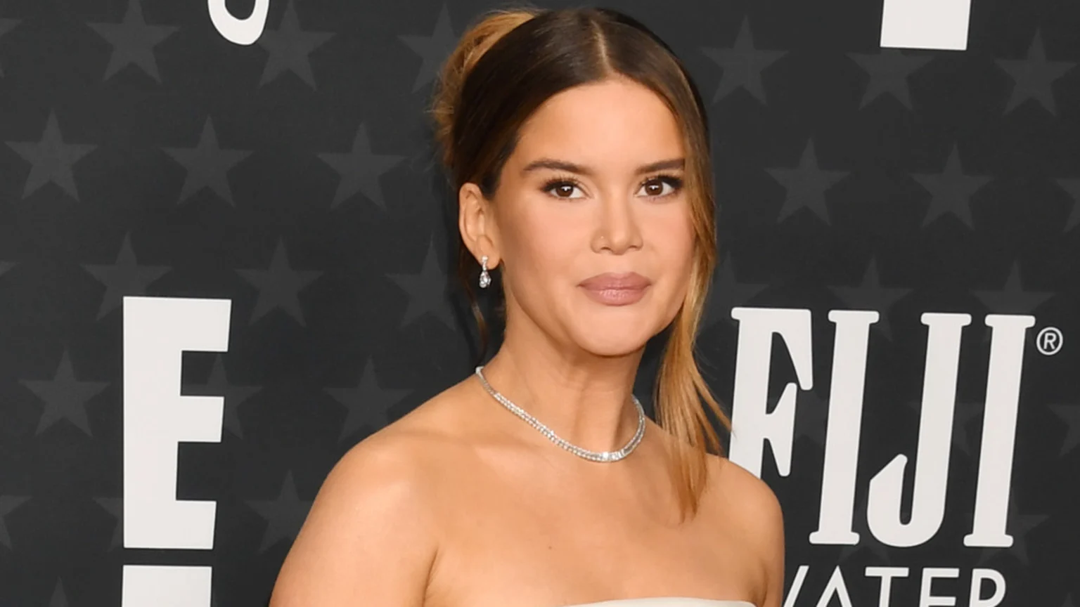Maren Morris, with her hair pulled back and wearing a strapless top and diamond jewelry, poses against a starry black background with partial "E" and "FIJI WATER" logos.