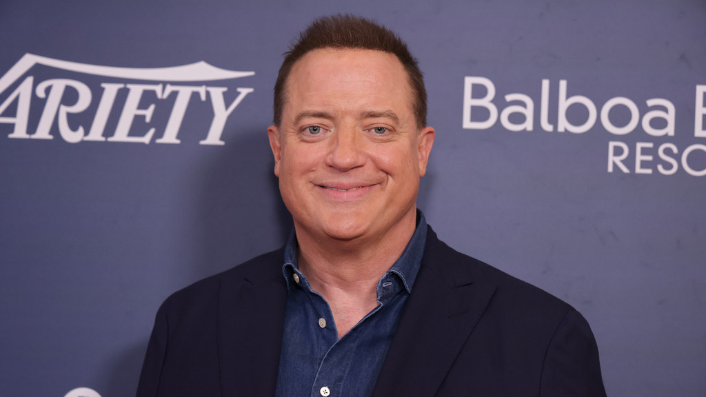 Actor Brendan Fraser smiles, wearing a dark blue suit jacket over a denim shirt, against a purple background with white "Variety" and "Balboa" logos.