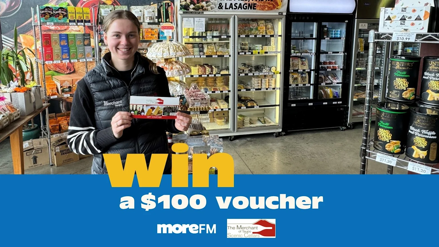 A smiling woman holds a gift voucher from "The Merchant of Taupo" in a store, with text overlay "win a $100 voucher" and logos for MoreFM and The Merchant of Taupo Scenic Cellars.