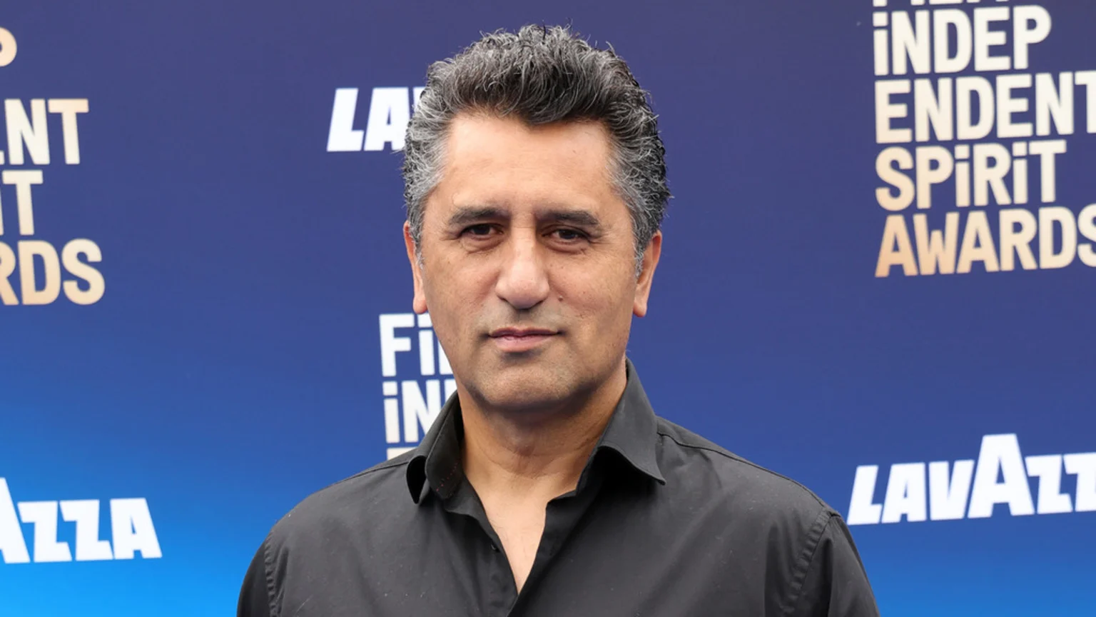 A man with grey hair and a black shirt poses in front of a blue background with "Independent Spirit Awards" and "Lavazza" text.